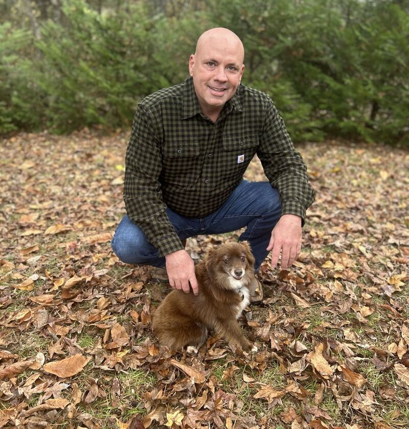 Mark Hickman outdoors in the fall leaves with his dog